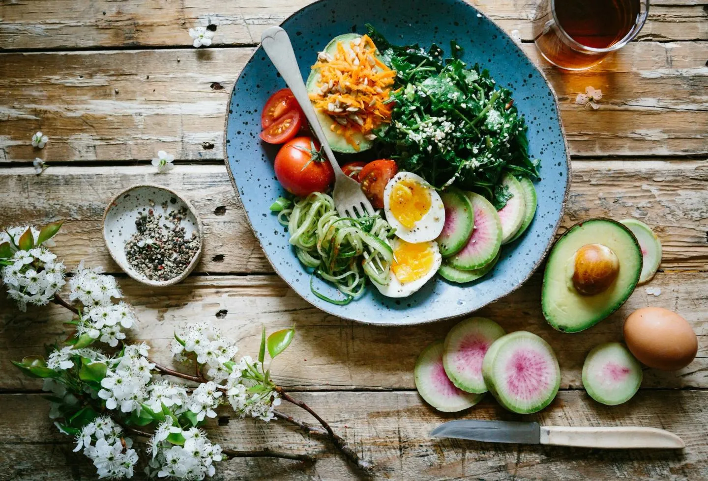 An overhead plate with egg, avocado, radish and mixed salad greens on a wooden surface